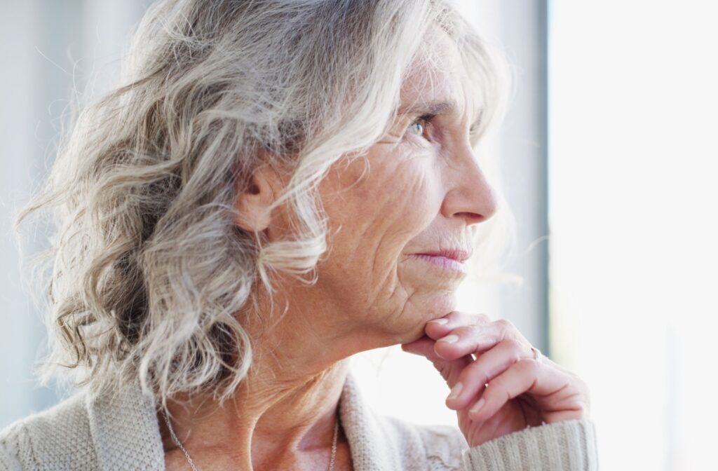 A close-up of an elderly woman's face looking out the window with her hand resting on her chin.